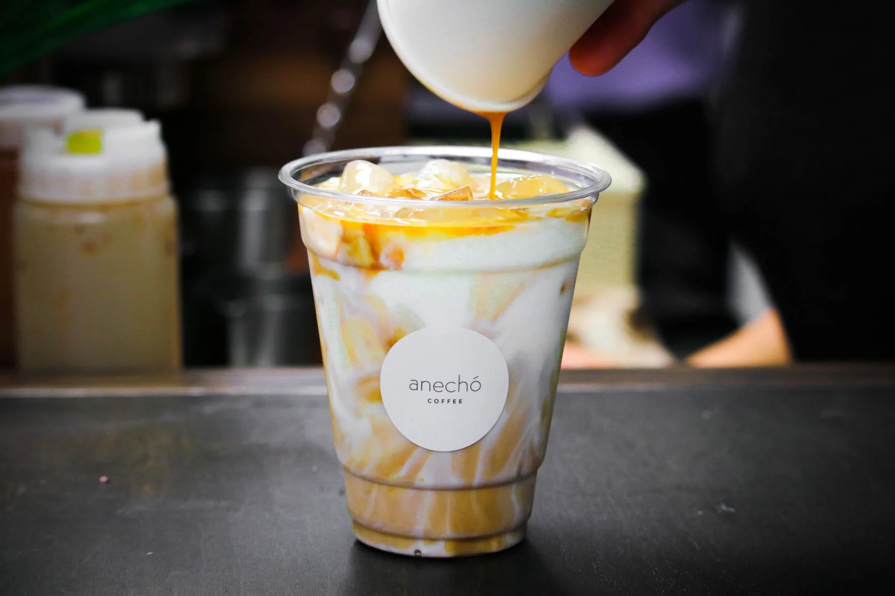 Barista finishing an iced latte in an Anechó branded cup at a client appreciation event